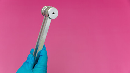 Blue Gloved Hands Holding tuning fork On pink Background, medical instruments in the hands of a...