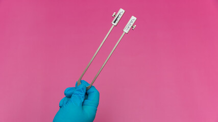 Blue Gloved Hands Holding tuning fork On pink Background, medical instruments in the hands of a...