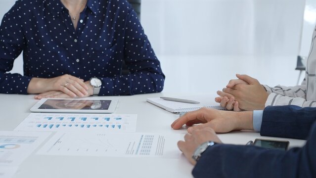 Business people examining and discussing financial documents, studying performance charts on paper and digital tablet during collaborative meeting in modern office