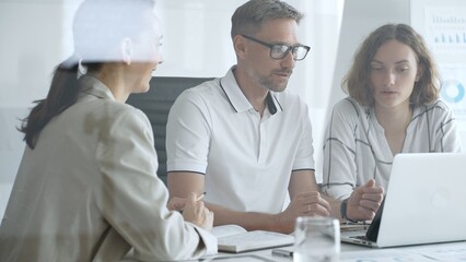 Professional team working together, reviewing digital analytics on laptop screen while strategizing corporate project details in modern workplace environment. Business people concept