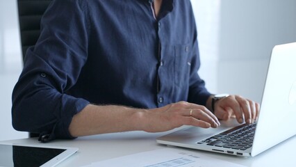 Obraz premium Professional businessman typing on laptop, surrounded by financial reports and digital tablet, working in contemporary corporate workspace. Business people concept