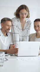 Obraz premium Professional team reviewing project data on laptop, working together in modern office environment, collaborating with focused corporate energy