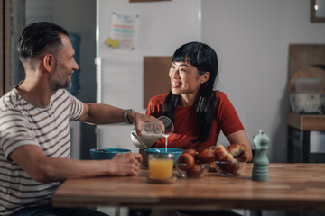 Happy couple having breakfast together in kitchen, pouring milk