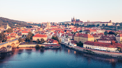 Fototapeta premium A breathtaking view of Prague at sunrise reveals the Vltava River and iconic Charles Bridge, with medieval buildings and Hradcany castle bathed in warm morning light, creating a serene atmosphere.