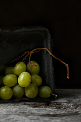A bunch of green grapes in a black cardboard produce box on a rustic wood table with balck background.