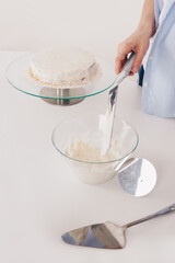 Young woman with slim hands decorates a chocolate sponge cake with a palette knife and butter cream on a special stand to assemble a delicious cake. Homemade chocolate sponge cake.