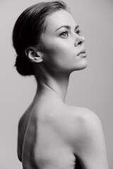 Elegant woman with a graceful posture, looking up thoughtfully against a soft grayscale background. Mood of contemplation and beauty captured in monochrome.