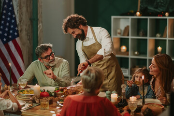 Family celebrating thanksgiving, father carving turkey at home dinner table with american flag
