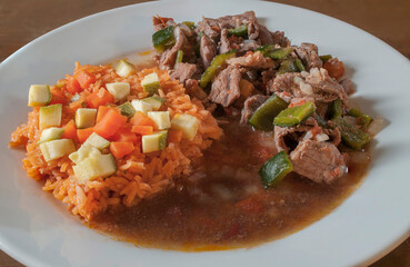 Tomato-spiced beef with chili and Mexican rice with zucchini and carrots on a white plate, as part of a Mexican diet