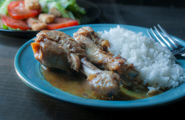 Chicken with oyster sauce with steamed rice on one side on a blue plate and salad in the background.