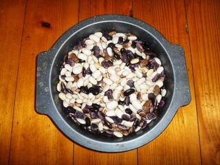 A close-up of a bowl filled with various colorful dry beans on a rustic wooden surface