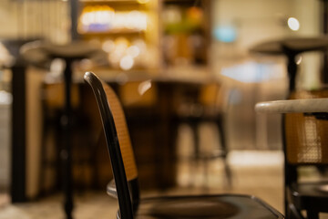 Stylish coffee shop interior with blurred bar counter in background, focus on wooden chair creating peaceful mood and warm evening ambience of modern urban restaurant or lounge space