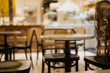 Modern cafe interior with empty marble tables and wooden chairs in soft evening lighting, showcasing hospitality design, cozy atmosphere and elegant restaurant or coffee shop environment
