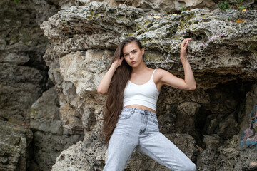 Beautiful woman in a white top and gray jeans poses on rocks in the mountains