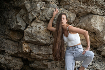 Young beautiful woman in a white top posing on rocks in the mountains