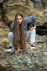Beautiful woman in a white top and gray jeans poses on rocks in the mountains