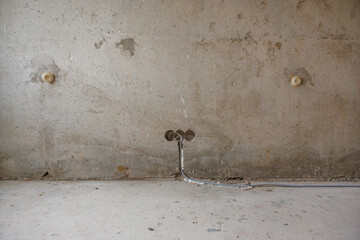 Bare concrete wall with visible imperfections, two circular outlets, exposed wiring, and a concrete...
