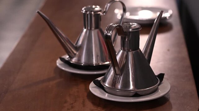 two fancy stainless steel olive oil dispensers on a wooden table at a restaurant