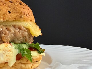 A large cheeseburger with tomatoes and greens on a white plate. Delicious, nutritious, and quick food.