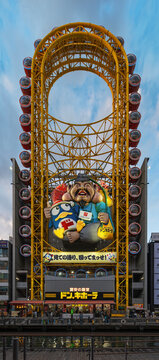 osaka, dotonbori - dec 6 2024: Landmark oval-shaped japanese ferris wheel of Don Quijote store feat penguin mascot Donpen with Ebisu god of fishermen and luck fishing a red sea bream along the canal.