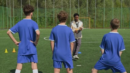 Back view shot of three preteen players stretching muscles while talented African American coach talking - Powered by Adobe