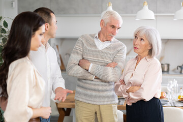 Young adult man presenting modest girlfriend to elderly parents, expressing disapproval and concern during tense meeting in family home