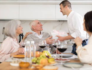 Smiling son giving a gift box to his father during cozy get-together with old parents in their house