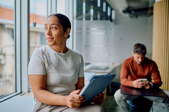 Businesswoman holding a digital tablet, looking out the window, contemplating future ideas in a modern office environment