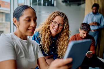 Young diverse business team members collaborating and smiling while working with a digital tablet in a modern office space