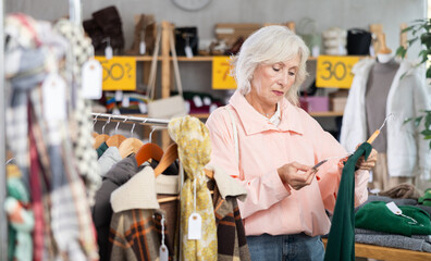 Mature woman near showcase examine goods, buying warm full length dress. Off line clothing store from retailer. Style and fashion type look, modern trends. Outlet, discount store...