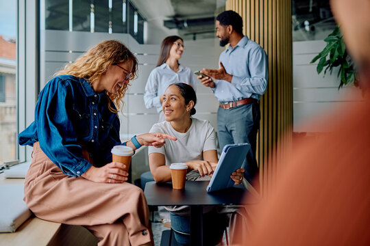 Diverse colleagues discussing ideas and smiling during a coffee break in a modern office, enjoying teamwork and informal interaction - Powered by Adobe
