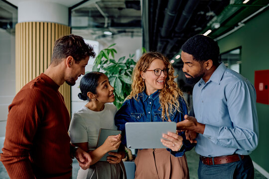 Four business colleagues collaborating on a new project standing in a modern office, analyzing data on a digital tablet
