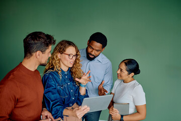 Diverse business team actively discussing ideas and collaborating on a project, using a digital tablet against green background