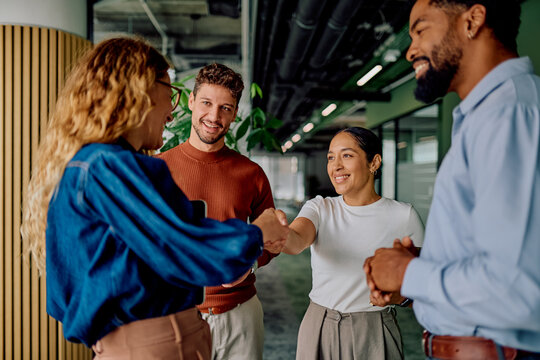 Diverse business people shaking hands, smiling at a successful agreement during a meeting in a modern office environment - Powered by Adobe