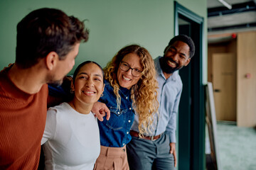 Diverse group of smiling business people standing together in an office hallway, showing teamwork and happy interaction