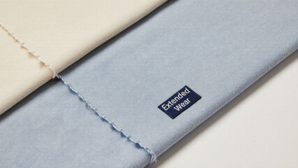 Minimal label tag sewn onto light blue folded fabric in angled view