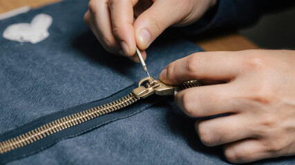 Hands repairing broken zipper on dark fabric using needle and thread