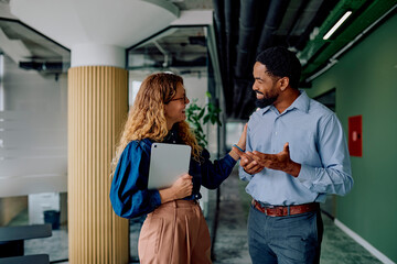 Diverse business colleagues talking and smiling during a discussion in a modern office hallway, showing teamwork and collaboration