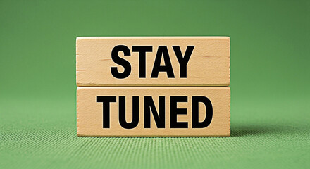 Wooden blocks spell out stay tuned against a green background for an upcoming announcement message