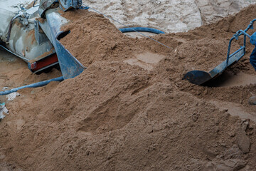 A pile of freshly moved sand with a metal chute, shovel, and blue hoses scattered, indicating ongoing work at an active construction site.