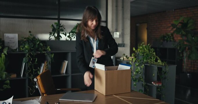 Young professional woman in business attire unpacks a moving box with office supplies during onboarding in a bright modern office symbolizing a fresh start and new career