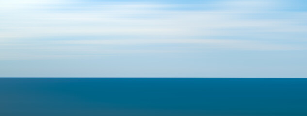 Obraz premium A wide panorama of the blue ocean against a white sky. The sky is clear and the ocean is calm.
