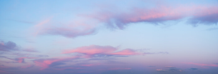 A wide panorama of a beautiful pink and blue sunset sky with clouds. The sky in pink and blue tones creates an atmosphere of calm and tranquility.