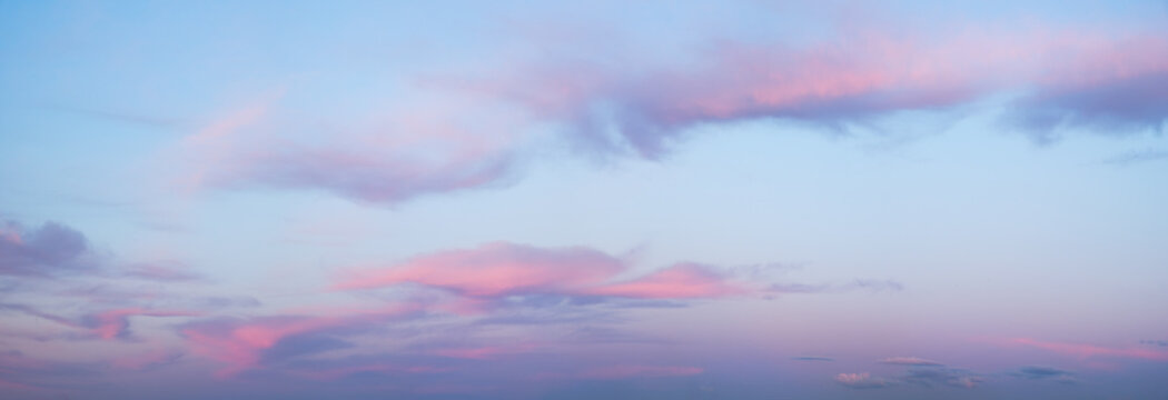 A wide panorama of a beautiful pink and blue sunset sky with clouds. The sky in pink and blue tones creates an atmosphere of calm and tranquility.