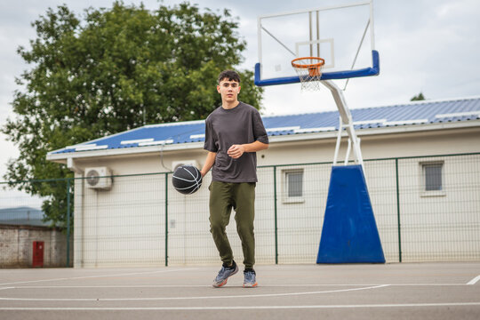Teenage boy dribbling basketball on outdoor court