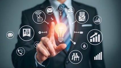 Obraz premium Businessman touching a glowing lightbulb surrounded by digital icons representing business concepts and technology.