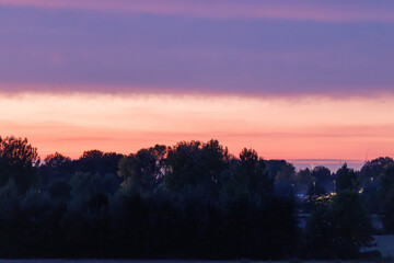 Dramatic purple and orange sunset sky over a dark treeline creating a peaceful and serene landscape, perfect for travel blogs or inspirational content, evokes tranquility and beauty