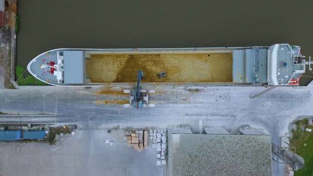 Aerial drone top down view of empty cargo ship being cleaned out by digger and crane, transportation and maritime economic shipping, Goole Port, River Ouse, England UK 