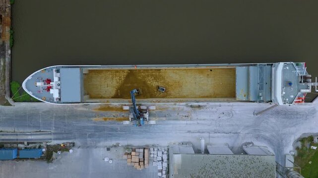 Aerial drone top down view of empty cargo ship being cleaned out by digger and crane, transportation and maritime economic shipping, Goole Port, River Ouse, England UK 