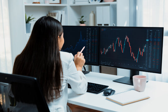 Young beautiful Asian businesswoman pointing with pen in exchange stock market on pc screen at back side view, analyzing profit at modern office, investing high profit valed in wealth. Stratagem.